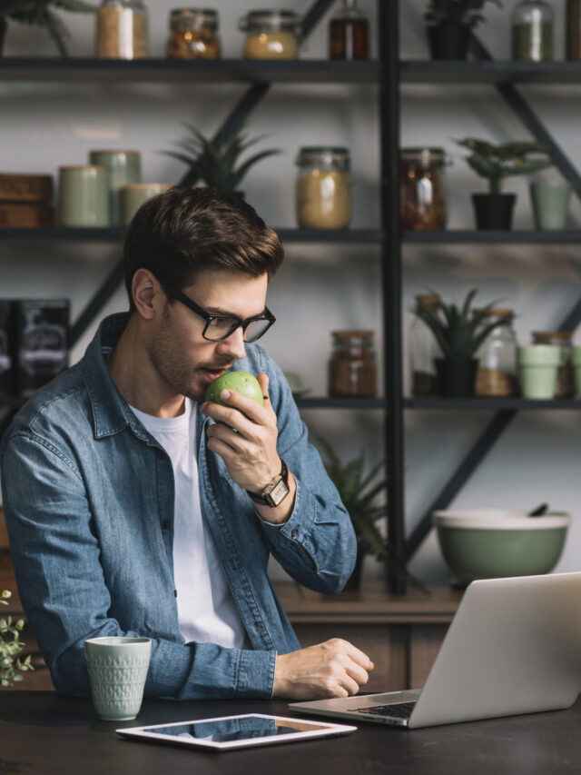 close-up-young-man-eating-green-apple-looking-digital-tablet