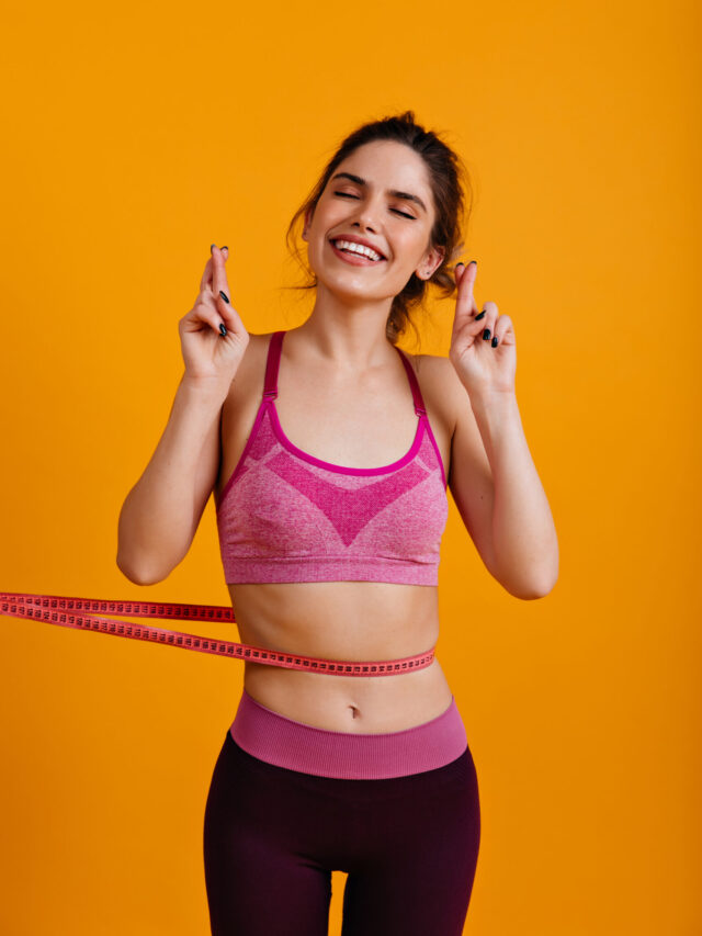 Studio photo of excited girl isolated on yellow background with measure tape. Good shape, sporty woman